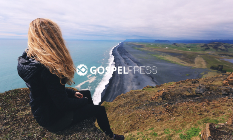 Moça sentada em um penhasco olhando para uma estrada à beira-mar em um momento de fé e reflexão em tempos de crise
