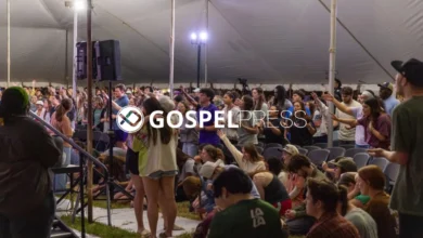 Jovens com as mãos levantadas em adoração durante um avivamento em tenda no campus de uma universidade do Texas, sob iluminação dramática.